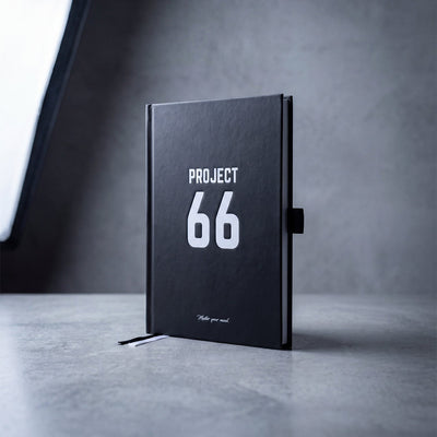 Black notebook with 'PROJECT 66' on a gray surface and background