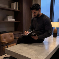 Man sitting at a desk writing in a notebook in a modern office setting.