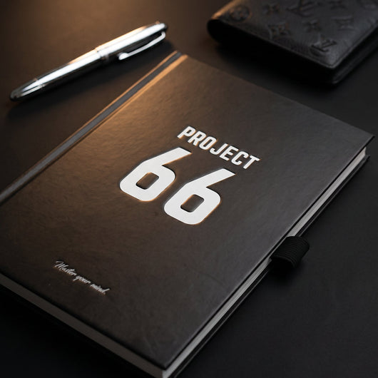 Black notebook with 'Project 66' on a dark surface, accompanied by a pen.